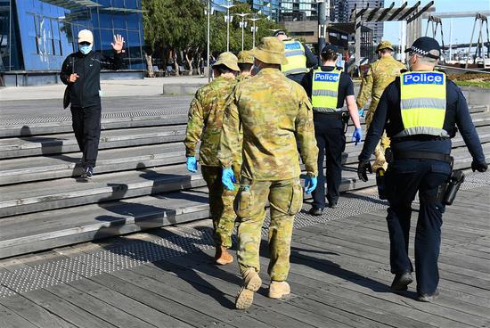 A man waves to a group of police and soldiers patrolling the Docklands area of Melbourne on Sunday, after the announcement of new restrictions to curb the spread of the COVID-19.