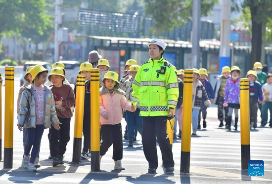 A traffic police officer escorts pupils across a street in Liuzhou, south China's Guangxi Zhuang Autonomous Region, Dec. 2, 2021. Dec. 2 marks the national traffic safety day in China. An event was held in Liuzhou to promote traffic safety. (Xinhua/Huang Xiaobang) 