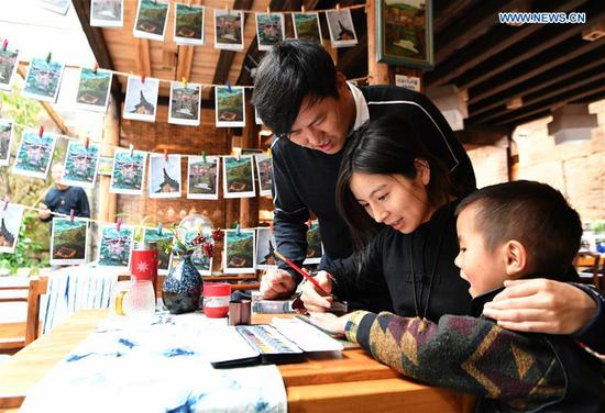 Hu Wenliang (1st L), a professional designer introduced to Longtan Village who started a cultural and creative space here, makes post cards with his family in Longtan Village of Pingnan County in Ningde City, southeast China's Fujian Province, Oct. 21, 2020. Longtan Village had been a provincial-level poverty-stricken village due to lack of arable land. Villagers went out for work one after another with many old buildings left in disrepair. In 2017, the county government launched a project to boost ancient villages through cultural and creative industries. The old houses, once forgotten, have been connected to public utilities, reinforced and decorated inside, with the ancient appearance of the village remained. Moreover, the renaissance here has attracted many people and college graduates outside the village to work here. Nowadays, more and more people come to visit Longtan since the village has become popular on the Internet. (Xinhua/Wei Peiquan)