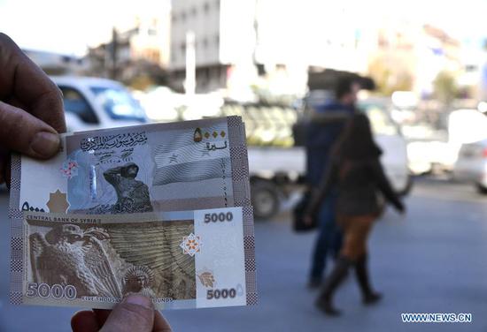 A Syrian shows new banknotes of 5,000 Syrian pounds in Damascus, Syria, on Jan. 24, 2021. The Central Bank of Syria on Sunday issued a new financial note for 5,000 Syrian pounds as part of the measures to confront inflation, according to the bank statement. (Photo by Ammar Safarjalani/Xinhua)