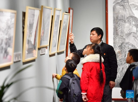 Wei Sancai (back) tells his experiences to students at his art exhibition in an art museum of Liuzhou City, south China's Guangxi Zhuang Autonomous Region, Dec. 5, 2021. An art exhibition of Wei Sancai, an art teacher, was unveiled on Friday in Liuzhou, displaying 100 art works on the theme of poverty alleviation and rural revitalization created by Wei during his tenure as a poverty alleviation official in Damiao Mountain. When he was assigned to Gaoqiang Village in Rongshui Miao Autonomous County of Liuzhou, Wei recorded the changes of the village with his paintings. In his spare time, he also took advantages of his profession to offer art classes for local children, providing them an access to the knowledge of arts. (Xinhua/Huang Xiaobang) 