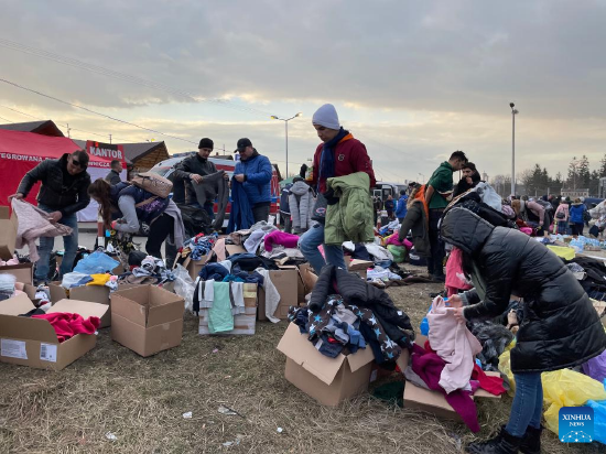 Photo taken with a mobile phone shows people selecting clothes donated by others in Medyka, Poland, Feb. 26, 2022. (Xinhua/Chen Chen)