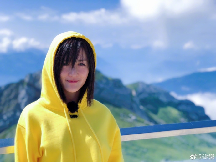 组图:谢娜穿黄色连帽衫拍旅途照片 比心微笑皮肤白皙透亮