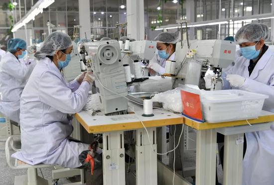 莆田双联鞋业有限公司的生产车间内工人在缝制口罩，图源新华社