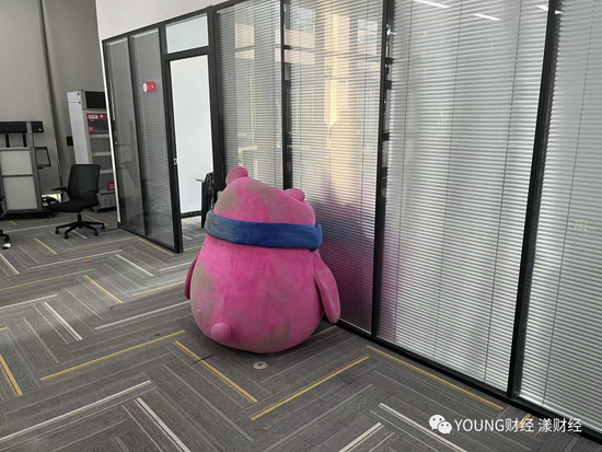 “深受员工喜爱”的吉祥物YOYO，被丢弃在地上，沾满尘土，它附近“每日优鲜便利购”办公室中仍有人开会