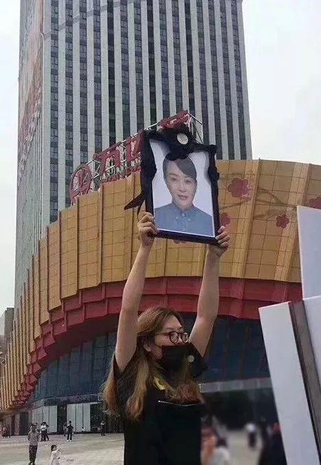  女儿举着妈妈徐毓的遗像，在南京万达茂门前讨要说法。图片来源：澎湃