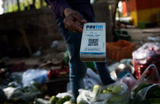 2017年4月12日，在印度新德里街头，一名蔬菜摊主手持Paytm二维码接受电子支付。印度Paytm在支付宝母公司蚂蚁金服的支持下，已经成为印度最大的移动支付平台。新华社记者毕晓洋摄