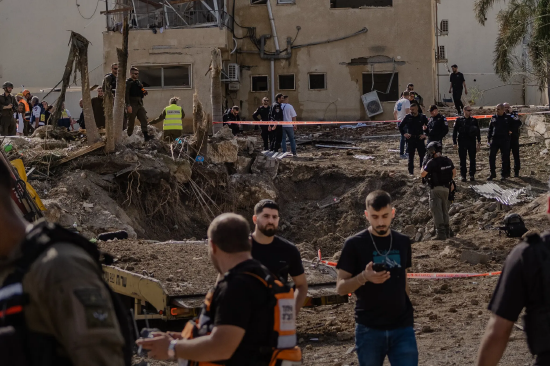 一群身着深色衣物的工作人员站在以色列境内一处地面弹坑旁，此前伊朗导弹在此发动袭击。周六，以色列埃什托尔镇袭击现场的应急救援人员。