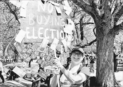 4月15日，来自美国佛罗里达的安德列亚·雷打着标语，上面贴满了自制的“美元”，调侃美国选举中的“金钱政治”。

　　本报记者 张朋辉摄