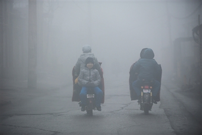 2016年12月22日7时45分，邯郸市区，一名学生倒坐在行驶的电瓶车上。当天早上，邯郸依旧笼罩在雾霾之中。