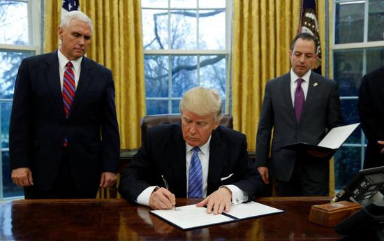 特朗普在副总统彭斯(左)和幕僚长普利巴斯注视下签署退出TPP命令