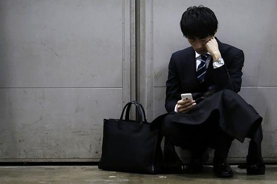 2015年3月8日，日本东京一场招聘会期间，一位求职者在角落看手机。图片来源：视觉中国