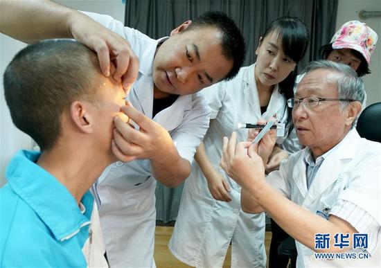 眼科专家、兰州普瑞眼科医院院长李晓林大夫（右）与张国文大夫（左二）、张晓艳大夫（左三）为高三学生罗进荣（左）进行检查（8月12日摄）。