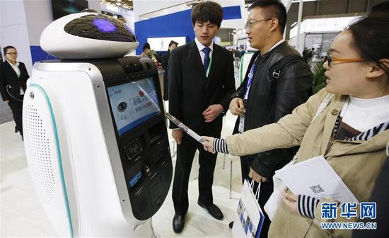 参观者在服务机器人展会现场向工作人员询问一款银行服务机器人的功能