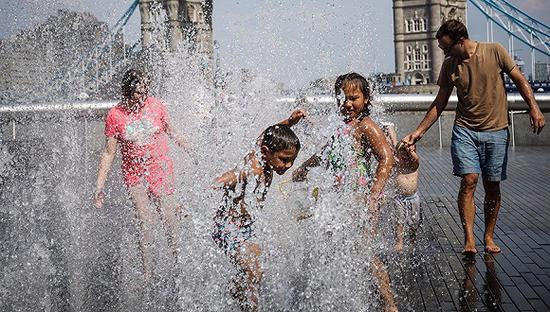 2018年7月26日，英国伦敦，高温天气，儿童在喷泉内戏水纳凉。图片来源：视觉中国