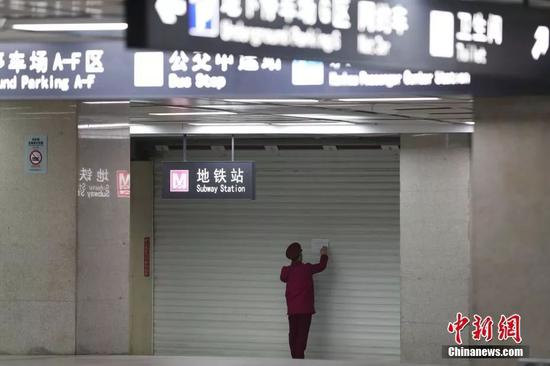 资料图：1月23日，武汉地铁暂停运营，一名工作人员在拉下的门帘上粘贴公告。中新社记者 张畅 摄