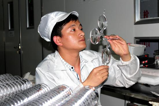 一名工人正在认真地检查刚生产出来的镜片是否存在瑕疵(刘默涵)