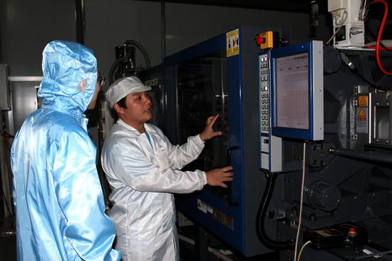 图为工作人员正在巡视PC镜片的生产机器(刘默涵摄)