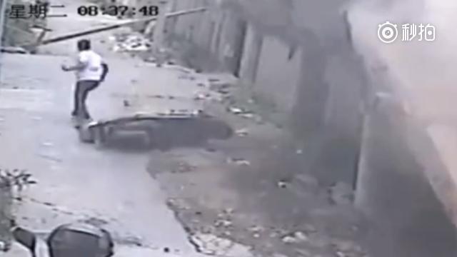 一名白衣男子骑着电动车准备掉头，这时，房屋突然坍塌，墙壁随即倒塌，白衣男...