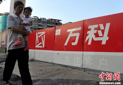 资料图:民众从万科某楼盘工地旁经过。中新社记者 张斌 摄