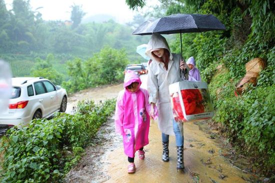 王心凌牵着结对小朋友的手冒着大雨前往建在山坡上的家