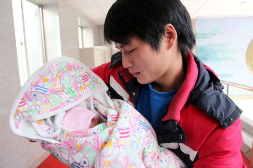 年轻小伙毛奎饶欣喜地从医生手中接过在早产病房接受护理42天的三女儿