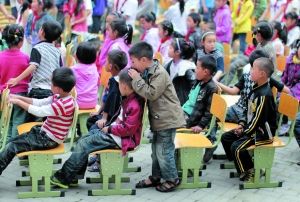 5月5日，小学生们在操场集合。一名小男孩的头被椅子磕到，同学在给他“吹气”。