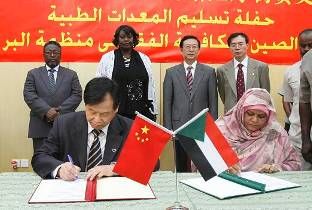 基金会杨青海副秘书长与塔哈夫人在捐赠协议上签字。后排左起：苏丹人道主义事务署专员阿卜杜拉赫曼，苏丹卫生部长舒卡娅，中国驻苏丹大使馆李成文大使，刘增先政务参赞。