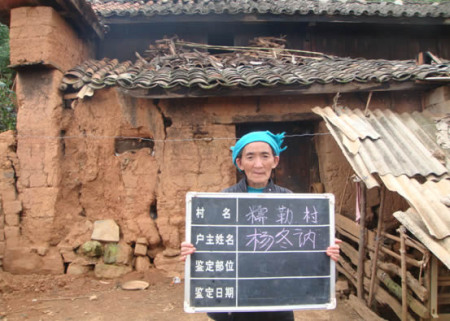 村民举着村委会提供的信息板站在自家危房门口