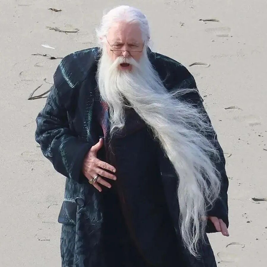 剧版《哈利·波特》“邓布利多”片场新照曝光，留着长白胡须，身穿宽大的长袍站在沙滩上