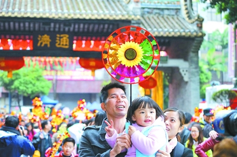昨日，一小女孩在父亲的怀抱里举着风车行通济。 　　/佛山日报记者张弘弢摄