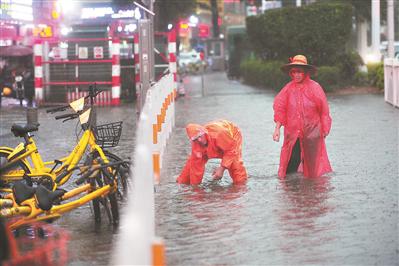 两名环卫工人冒雨清理堵塞的下水道口。