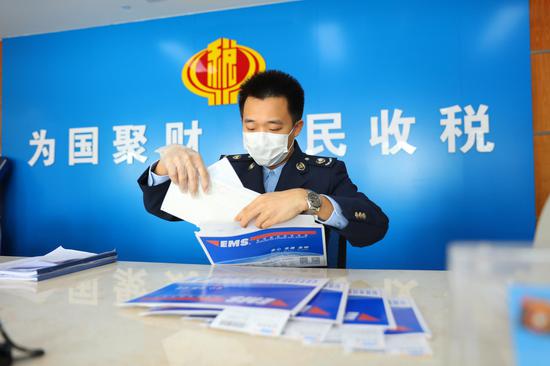 (图为税务青年邓振迪为纳税人包装好发票,等待邮政工作人员揽件)