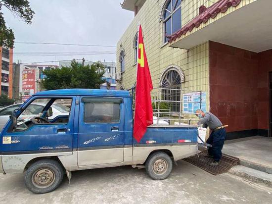 邓伯贤插着党旗的送餐车。他驾驶着它,坚持28天,每天送三餐走六趟,行程120公里,把一盒盒热饭,送到荷花镇9个检疫检查站的工作人员手上。