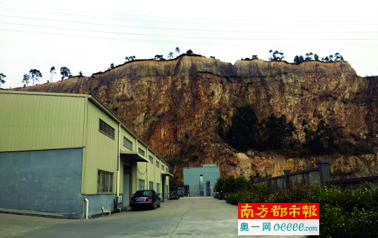 开山形成近百米高的峭壁,山脚下有工厂正在生产运营。南都记者 韩成良 摄