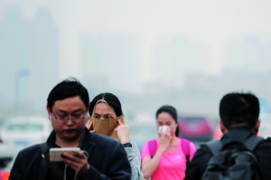 广州大桥上，雾霾让汽车和远处的高楼变得朦胧，一名女子用纸袋遮住口鼻。信息时报记者 陈引 摄