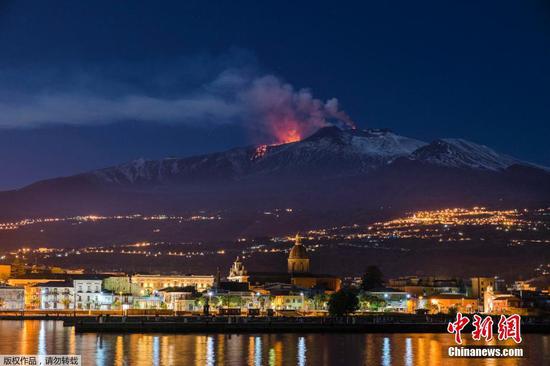 当地时间4月11日，意大利埃特纳火山持续喷发，被白雪覆盖的火山与山下码头灯光相映成辉。