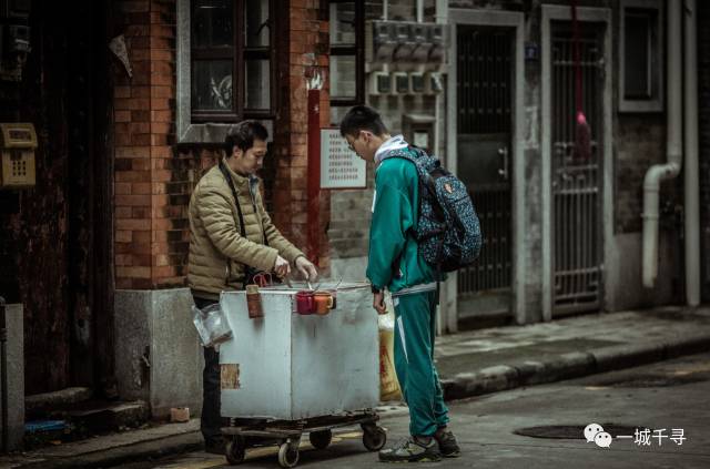 广州老街，一名穿校服的学生站在卖小吃的推车前。