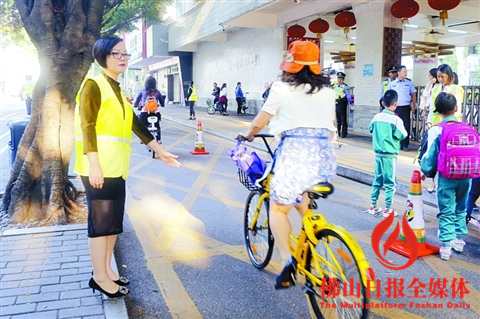 在燎原路二十五小门前,“警家校”护畅队队员指引骑车者经过。/佛山日报见习记者董倩倩摄