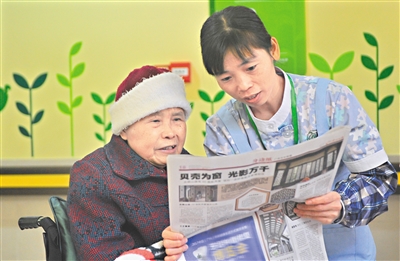 广州市松鹤养老院，护理员陪老人看报纸（资料图片）。 广州日报全媒体记者廖雪明 摄