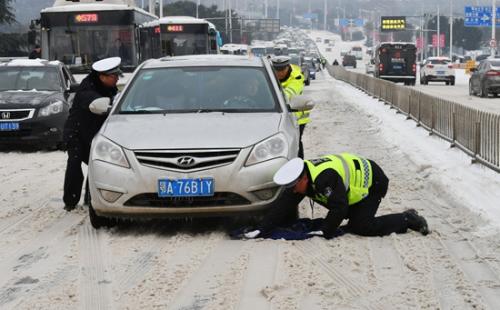 1月27日,在湖北省武汉市江汉一桥桥面,民警将衣服铺垫在雪地上协助推车。金思柳/摄(新华社发)