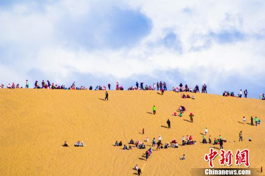 资料图:2017年“五一”小长假期间,游客登上甘肃敦煌鸣沙山月牙泉观赏大漠风光。 王斌银 摄