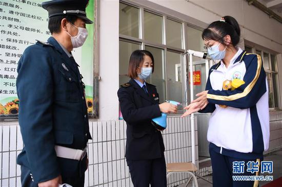 4月15日,兰州市第二十八中学“健康副校长”曹琴(中)在校门口为学生进行消毒。新华社记者 陈斌 摄