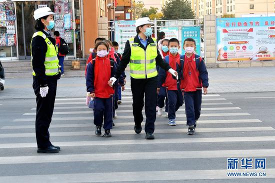 10月28日下午,民警手拉手护送小学生走过“斑马线”。新华网发(郑耀德 摄)