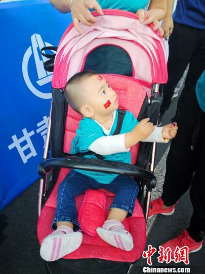图为小宝宝身穿幼儿定制版运动服,在童车里摇旗呐喊。 史静静 摄