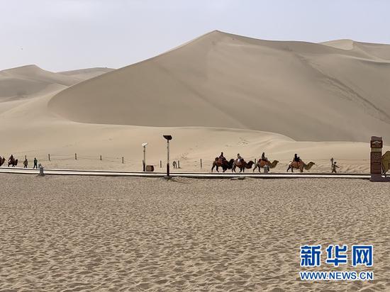 敦煌鸣沙山月牙泉景区内,游客骑着骆驼感受沙漠之美。新华社记者 李杰 摄