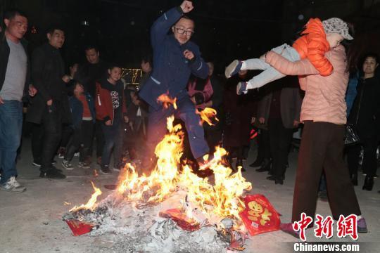 图为大人抱着小孩跳火堆“燎疳”。 郑兵 摄