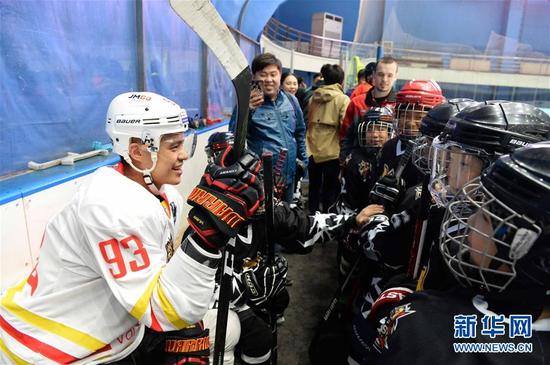 这是2017年4月20日,大陆冰球联赛(KHL)北京昆仑鸿星万科冰球龙队华裔球员袁俊杰(左)与冰球小学员们交流。新华社记者 王凯 摄