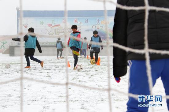 正在雪地里练习踢足球的孩子们。新华网发(丁凯 摄)