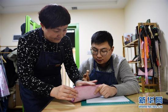李霞(左)在工作室指导顾客打磨皮具(1月12日摄)。 新华社记者 范培珅 摄